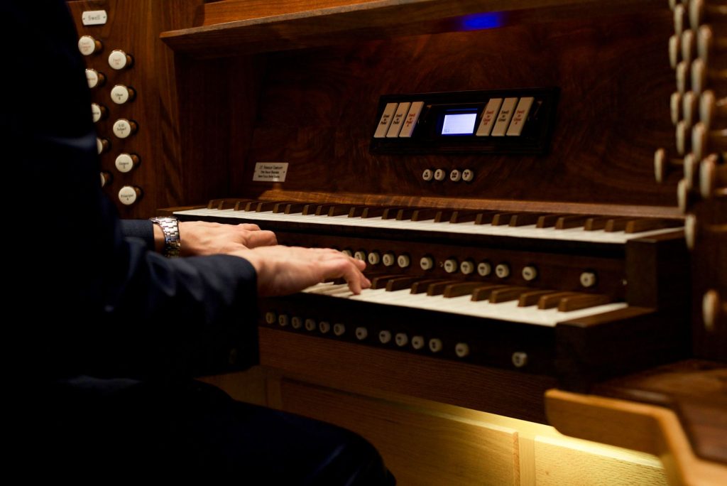 Mains d'un organiste sur les claviers d'un orgue d'église, registres et tirants de jeux visibles