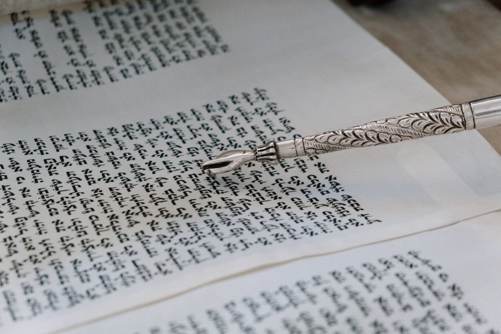 Yad d’argent en forme de main index tendu, posé sur le texte hébreu d’un rouleau de Torah