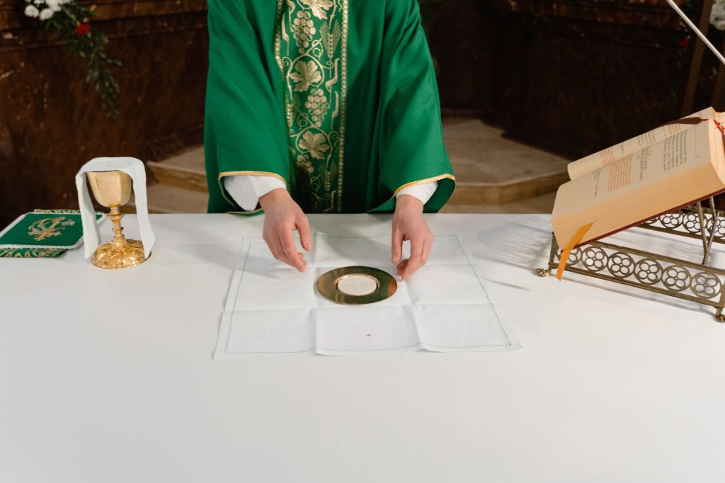 Prêtre catholique en chasuble verte préparant le pain eucharistique à l’autel